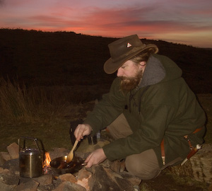 Bushcraft cooking over an open fire. A small billy can of rice boils while I brown the meat for a green curry.